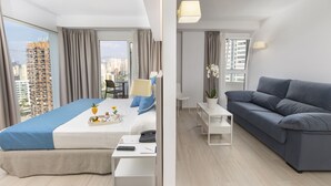A modern hotel room with a large bed, a sofa, a small table, and a view of the cityscape. -  Hotel Rosamar Benidorm (Benidorm)