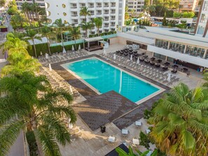 A rooftop pool with sun loungers and umbrellas, surrounded by palm trees and a building with balconies. -  Hotel Rosamar Benidorm (Benidorm)