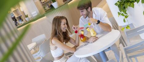 Una pareja cenando en una mesa blanca en un restaurante moderno y bien iluminado, con una barra al fondo.