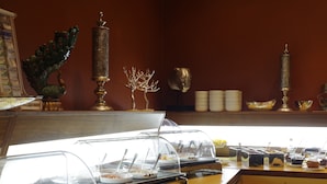 Zona de bufé con diversas opciones de comida y una pared decorativa con un pavo real y una escultura de cabeza.