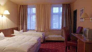 A hotel room with two beds, a desk with a television, a chair, and a window with curtains.