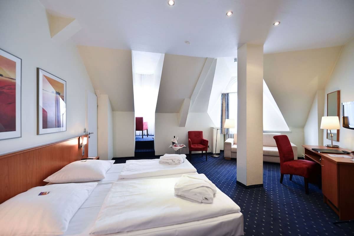 A hotel room with a large bed, a desk, a chair, and a view of the outside.
