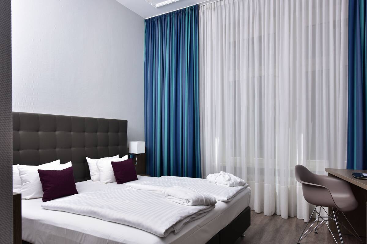 A hotel room with a large bed, a desk, and a chair.