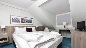 Habitación de hotel con cama, mesitas de noche, escritorio con computadora, televisor y ventana con persianas.