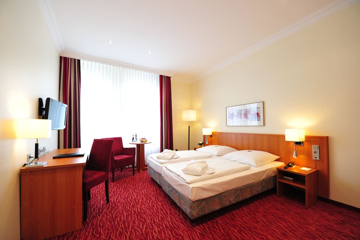 A hotel room with two beds, a desk with a computer, a chair, a small table, and a TV.
