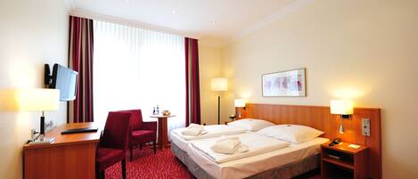 A hotel room with two beds, a desk with a computer, a chair, a small table, and a TV.