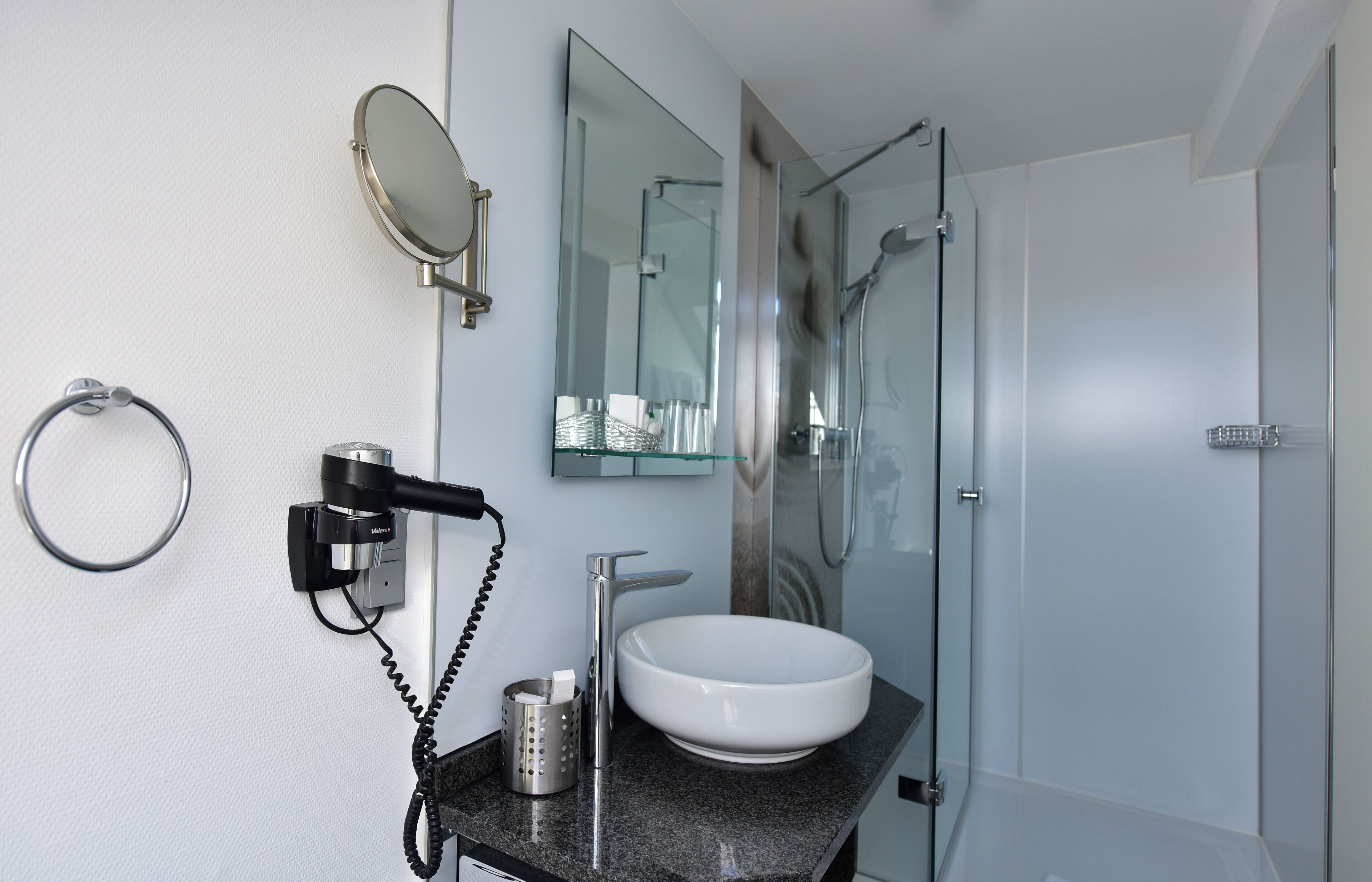 Une salle de bain moderne avec un lavabo blanc, une douche en verre et un miroir au-dessus du lavabo.