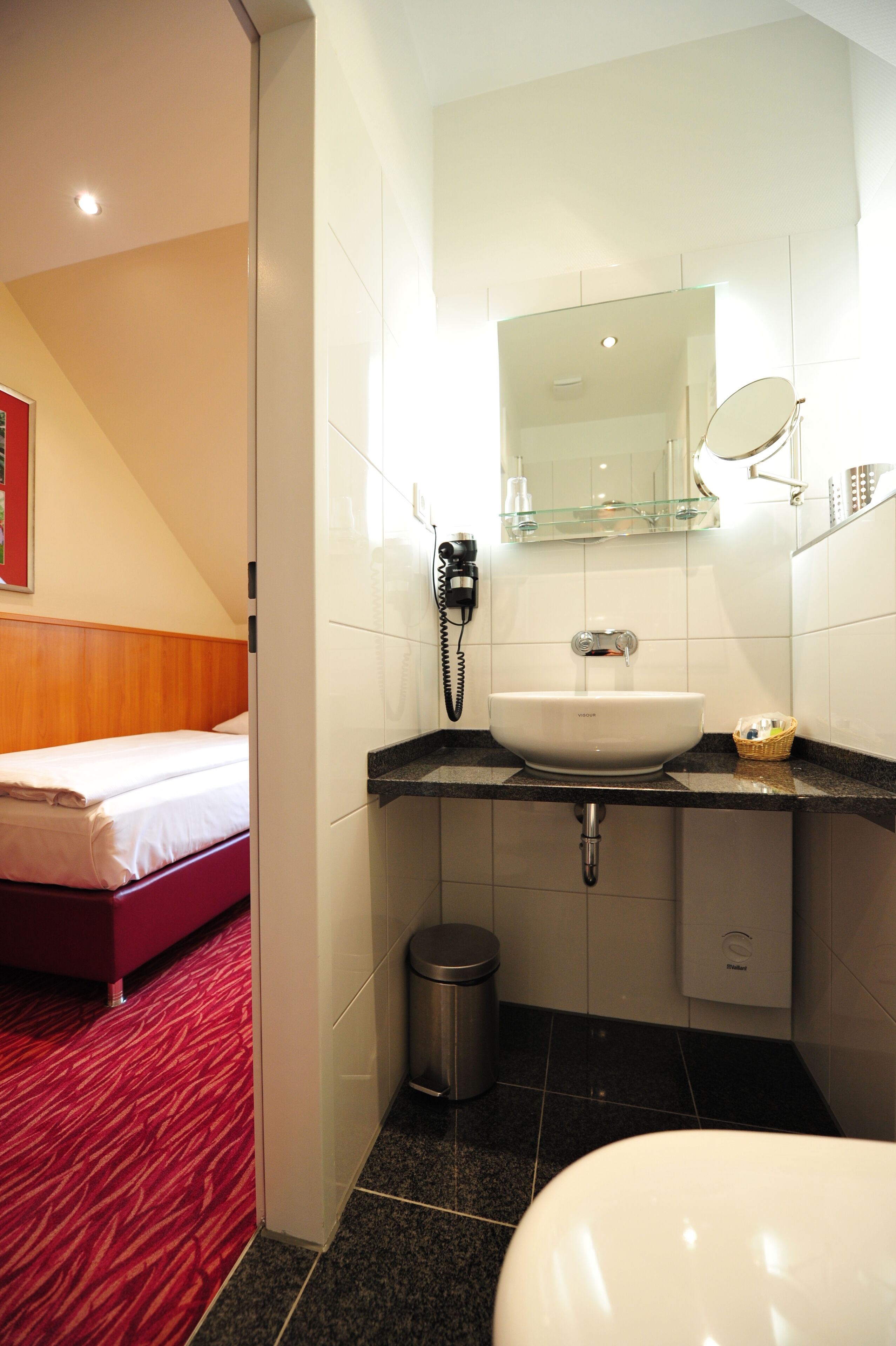 A hotel bathroom with a white sink, a mirror, a telephone, and a trash bin.