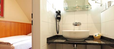 A hotel bathroom with a white sink, a mirror, a telephone, and a trash bin.