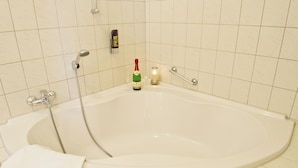 A bathroom with a large bathtub, a handheld showerhead, a bottle of champagne, and a candle. - Hotel Thüringer Hof (Jena)