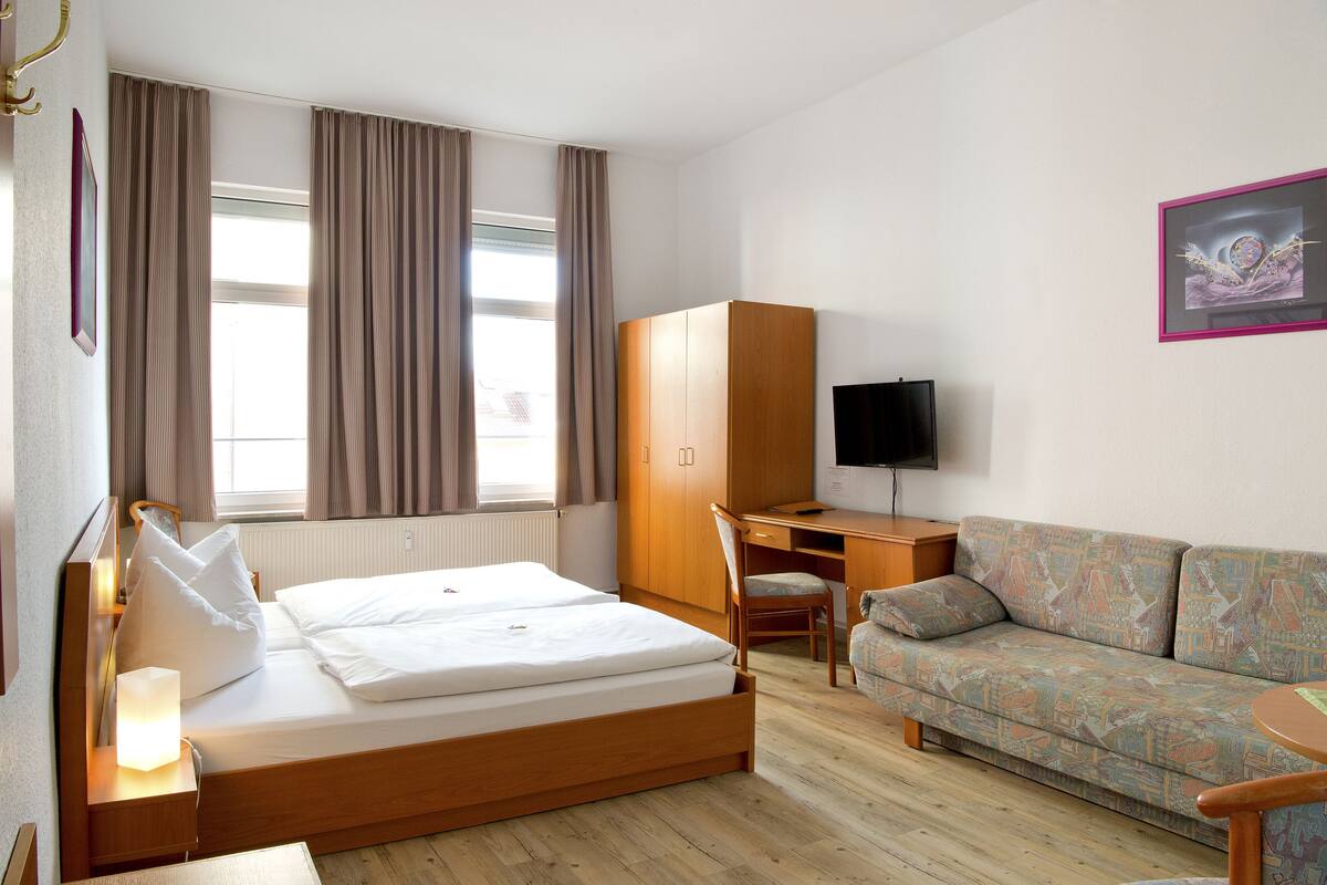 Habitación de hotel con cama, escritorio, sofá y televisor.
