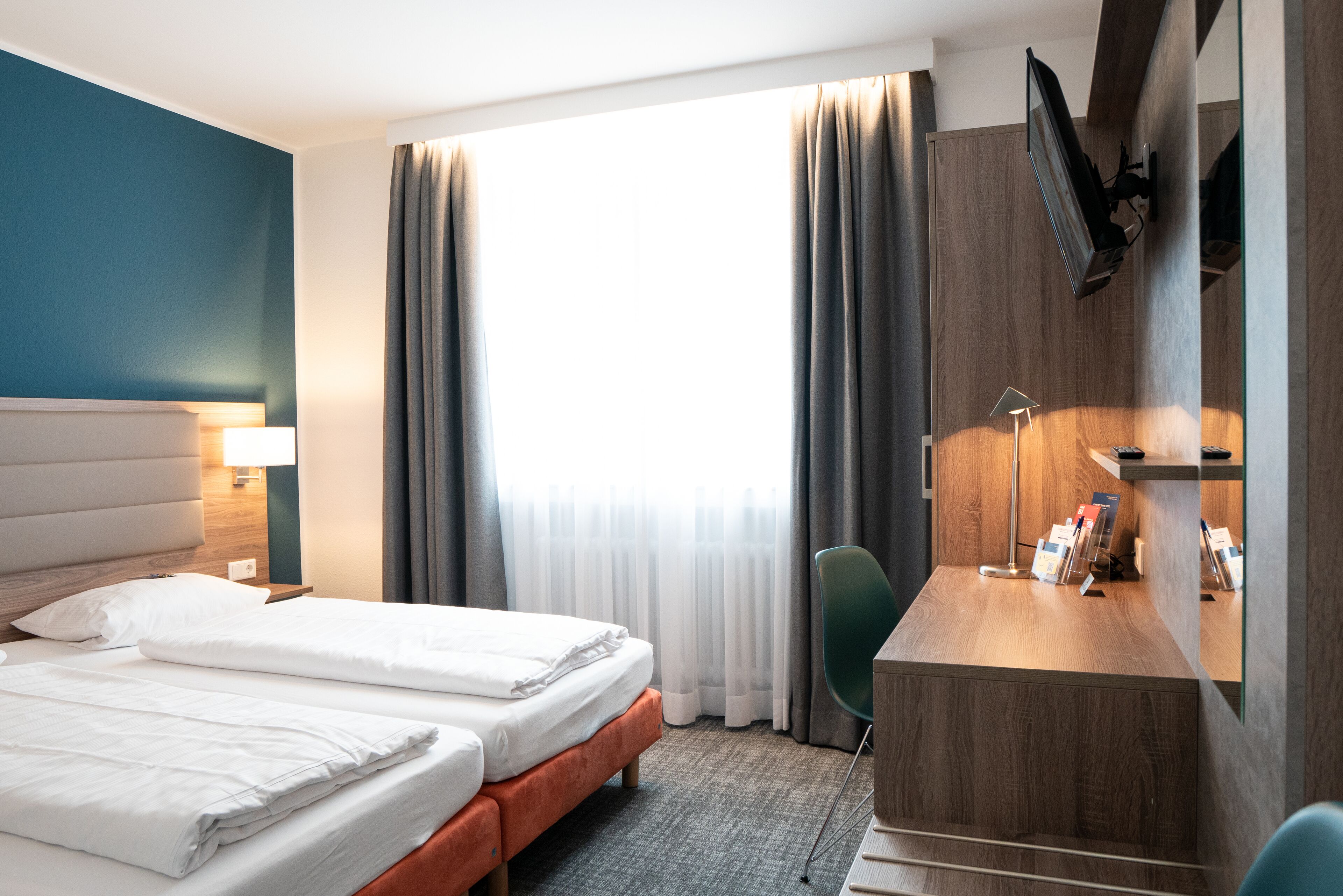 A hotel room with a bed, a desk, a chair, and a TV mounted on the wall.