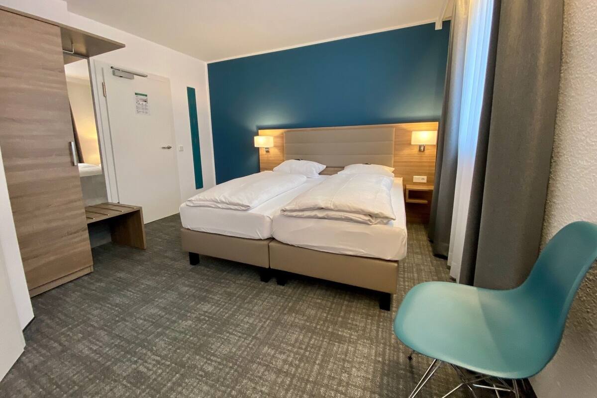A hotel room with a double bed, a desk, a chair, and a blue accent wall.