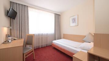 Habitación de hotel con cama, escritorio y silla, televisor montado en la pared y ventana con cortinas.