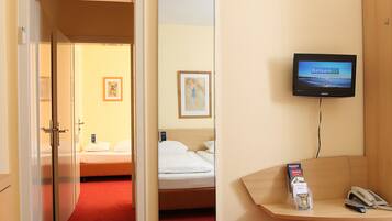 A hotel room with a bed, a desk with a phone and a magazine, a TV on the wall, and a mirror.