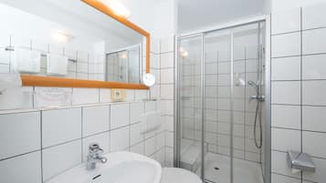 Un baño con lavamanos, inodoro y ducha con mampara de vidrio.