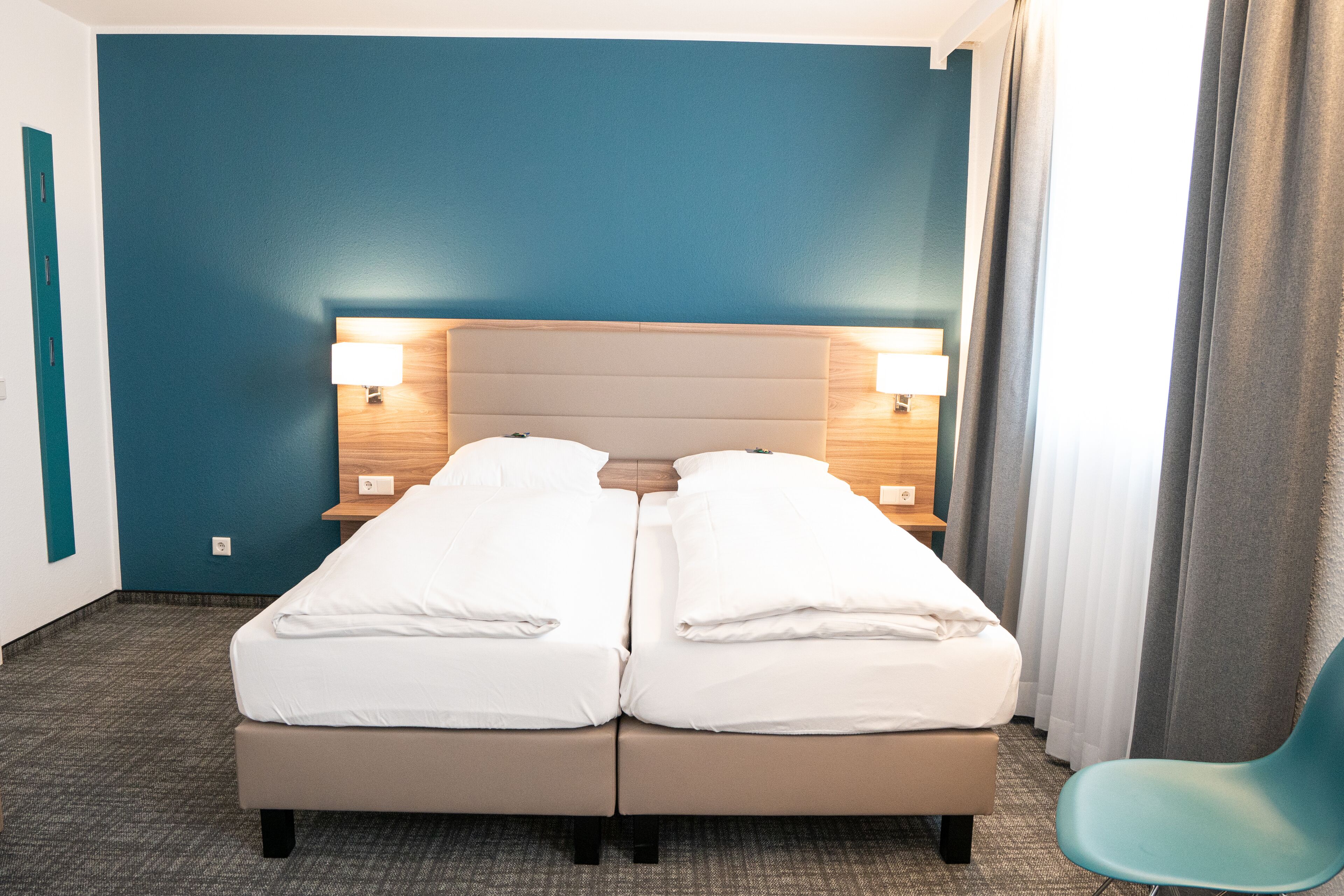Una cama doble con dos mesitas de noche, cada una con una lámpara, en una habitación con paredes color turquesa y una alfombra gris.