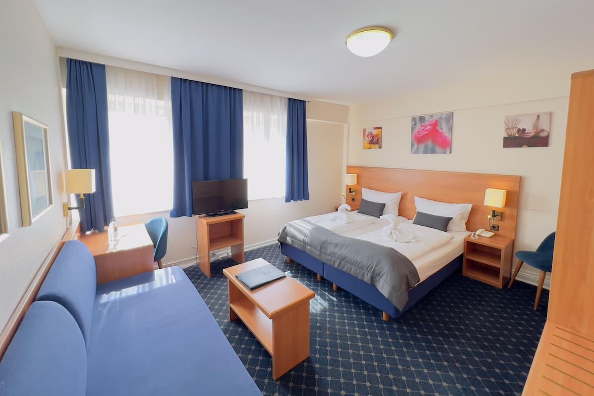 Una habitación de hotel con una cama, televisión, escritorio, silla y sofá.
