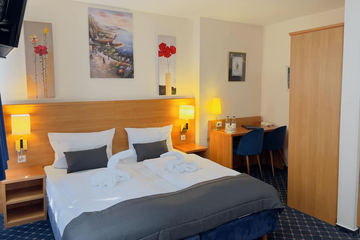 Una habitación de hotel con una cama, dos mesitas de noche, un escritorio con silla y obras de arte en las paredes.