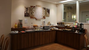 A breakfast bar with various food items and beverages, a coffee machine, and a wall decoration.