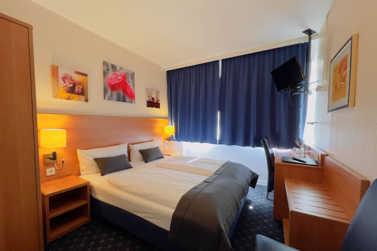Una habitación de hotel con una cama grande, mesitas de noche, un escritorio, un televisor y obras de arte en las paredes.