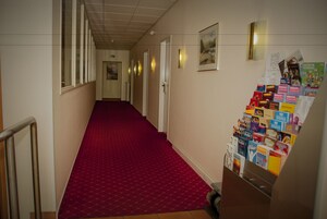 Ein Hotelgang mit rotem Teppich, Türen sowie einer Auswahl an Büchern und Zeitschriften.