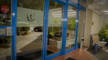 L’entrée d’un hôtel avec des portes en verre et un cadre bleu, une allée pavée et un banc à l’extérieur.