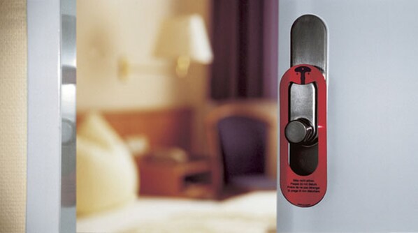 Puerta de una habitación de hotel con cerradura de llave electrónica y un sujetador de llavero rojo con texto.