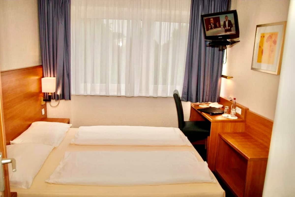 Una habitación de hotel con cama, escritorio, silla, televisor y ventana con cortinas.