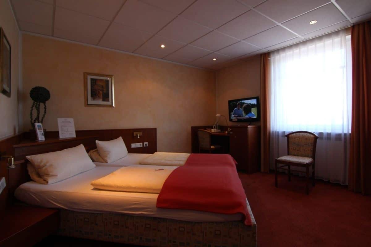 Hotellihuone, jossa on sänky, televisio, työpöytä ja tuoli.