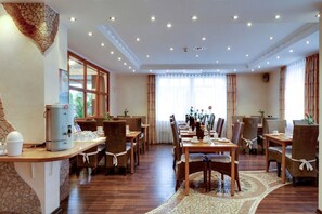A hotel dining area with wooden tables and chairs, a coffee machine, and large windows with curtains. - Hotel Heide Residenz (Paderborn)