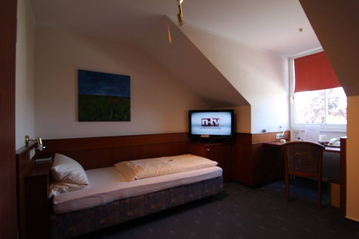 Hotellihuone, jossa on sänky, työpöytä, tuoli, televisio ja taulu seinällä.