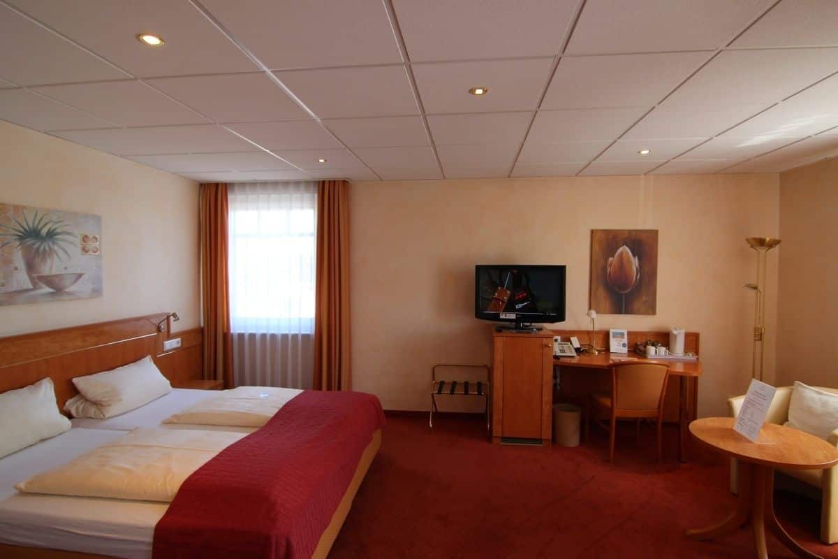 Hotellihuone, jossa on suuri sänky, työpöytä tuolilla, televisio ja pieni pöytä.