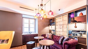 A cozy room with a plush red sofa, a yellow armchair, two small round tables, and a bookshelf filled with books and decorative items. - Premier Inn Passau Weisser Hase (Passau)