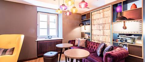 A cozy room with a plush red sofa, a yellow armchair, two small round tables, and a bookshelf filled with books and decorative items.