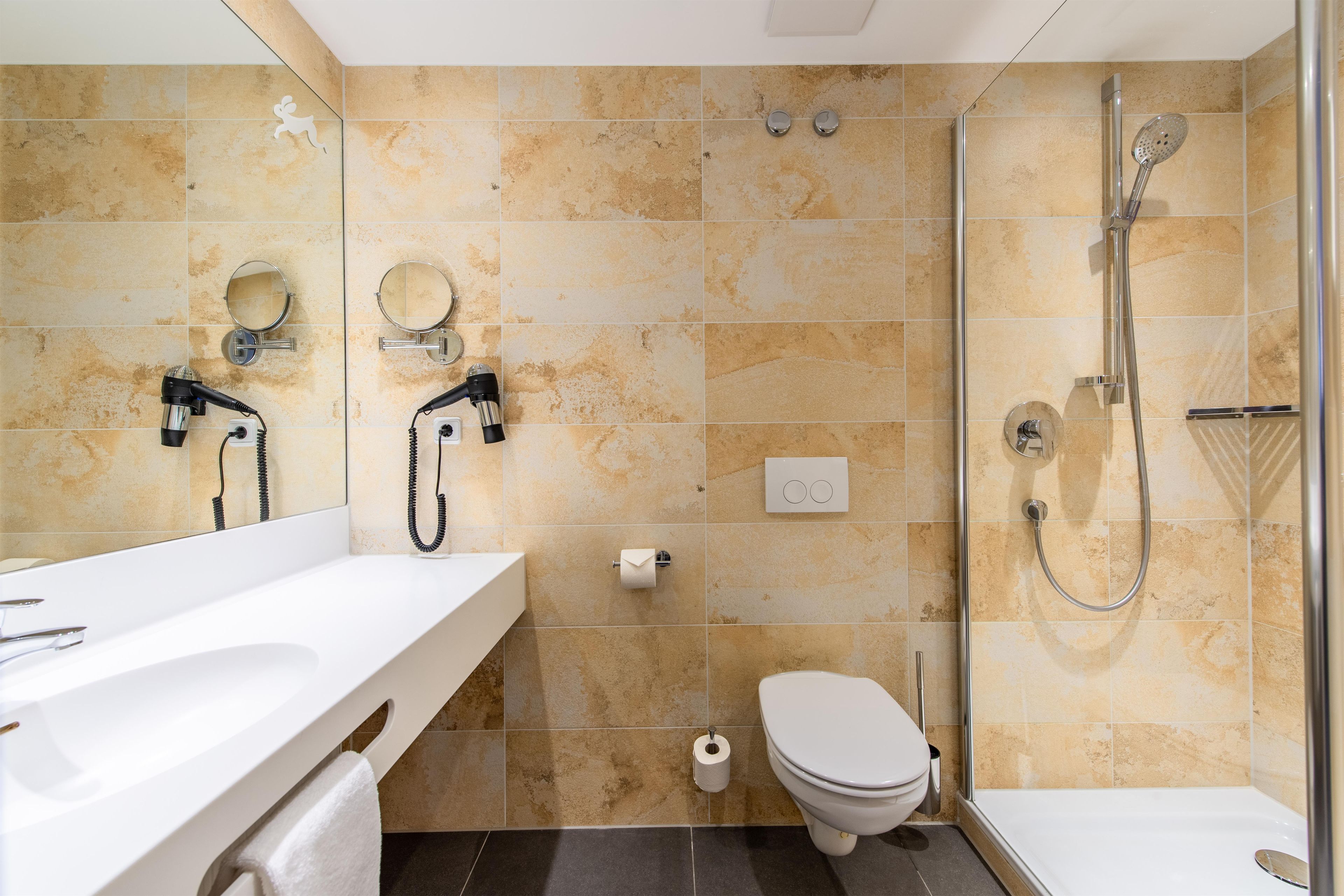 Une salle de bain avec douche, toilettes et deux lavabos avec miroirs.