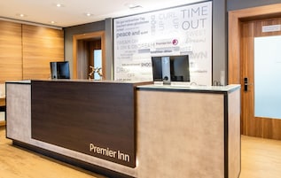 A hotel reception desk with a sign reading 'Premier Inn' and a wall with motivational phrases.