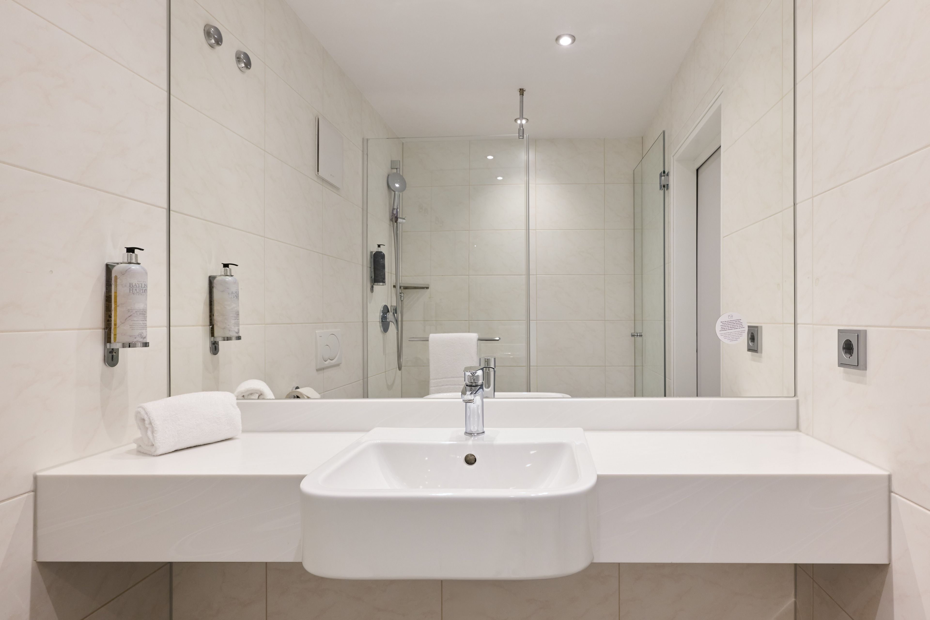 Un baño moderno con un espejo grande, un lavamanos blanco y una cabina de ducha de vidrio.
