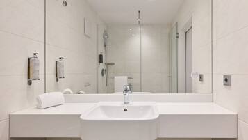 Un baño moderno con un espejo grande, un lavamanos blanco y una cabina de ducha de vidrio.