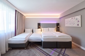 A hotel room with two single beds and one double bed, a large window with curtains, a wall clock, and a carpeted floor.