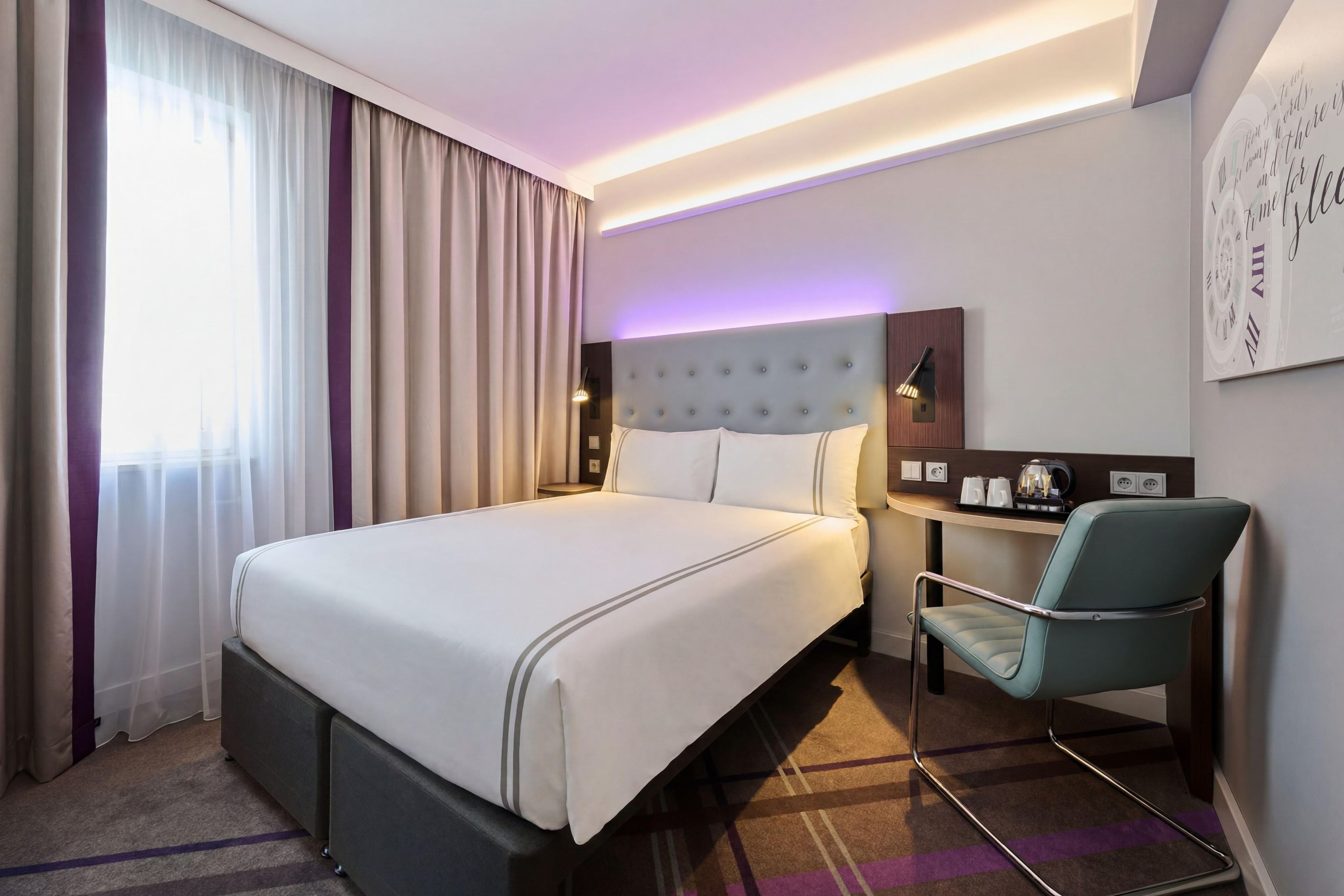 Ein Hotelzimmer mit einem großen Bett, einem Schreibtisch mit Stuhl und einer Wanduhr.