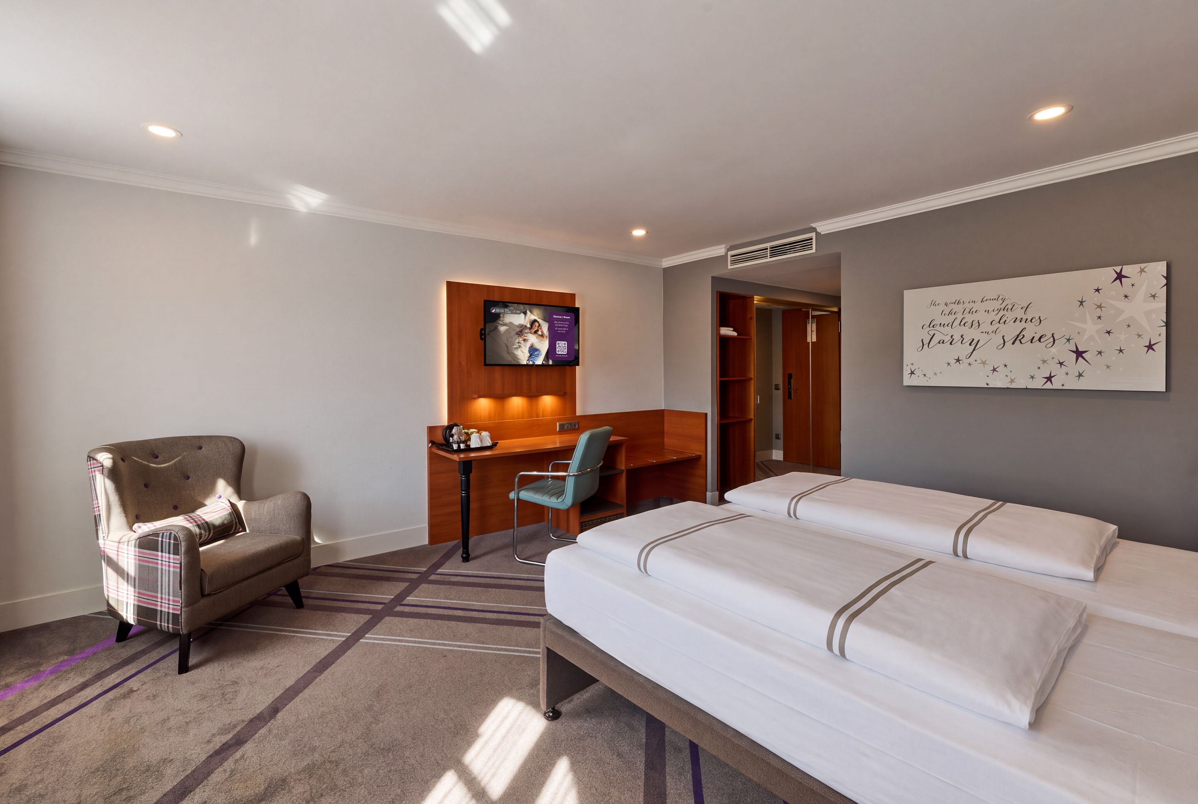 Habitación de hotel con cama, escritorio, silla, televisor y armario.