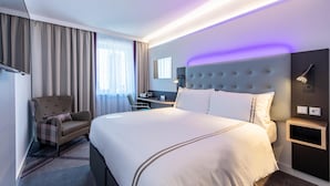 Habitación de hotel con una cama grande, un escritorio, una silla y cabecera con iluminación integrada.