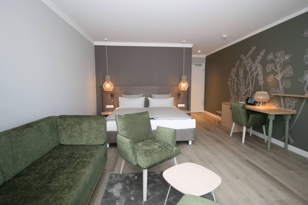 A modern bedroom with a bed, green upholstered furniture, a desk, and a wall with floral patterns.