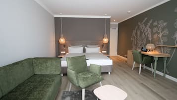 Un dormitorio moderno con cama, muebles tapizados en verde, un escritorio y una pared con motivos florales.