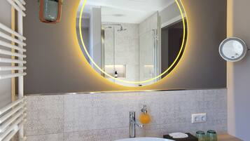 A modern bathroom with a large oval mirror, a white sink, and a glass shower enclosure.