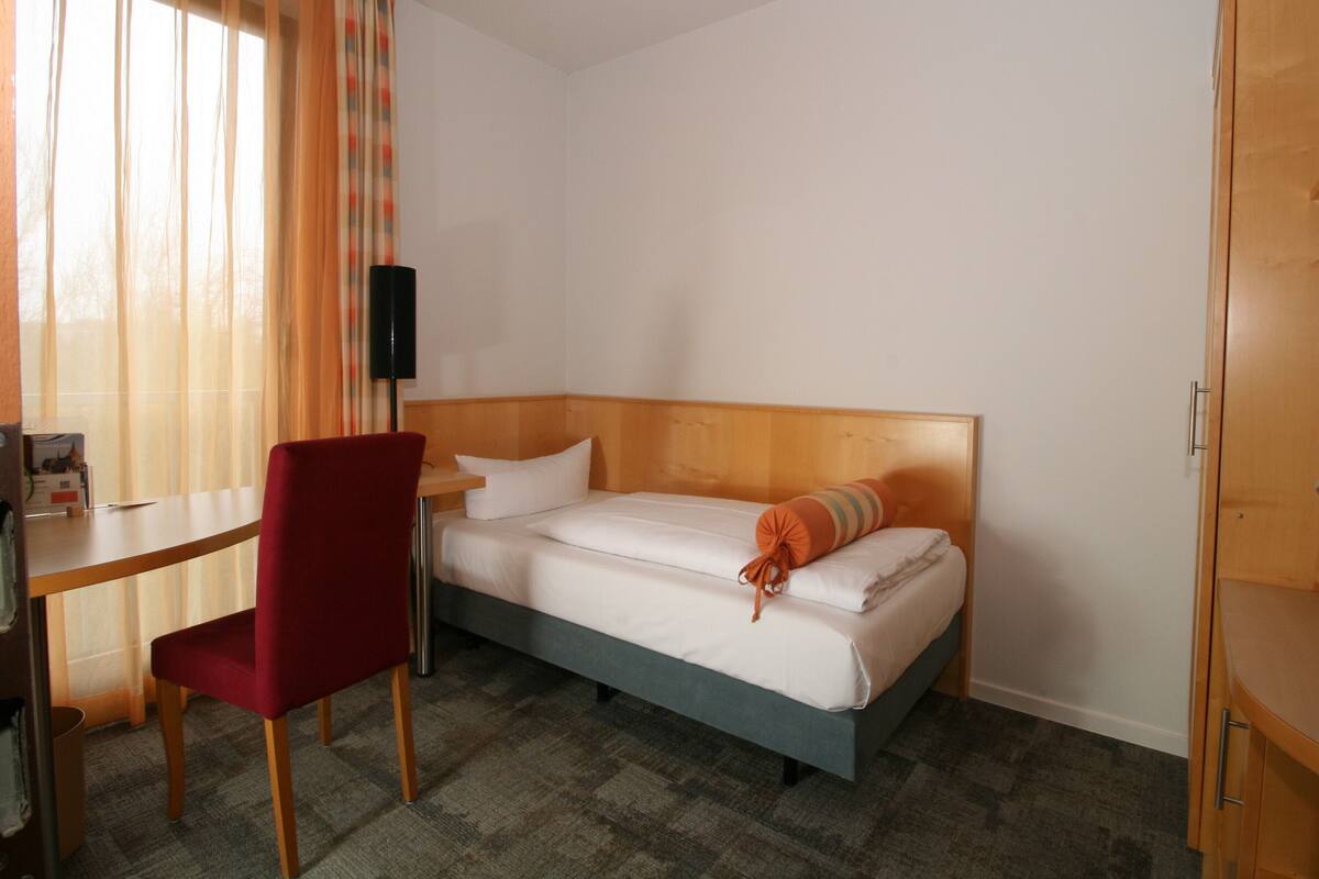 A hotel room with a single bed, a desk, a chair, and a wardrobe.