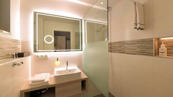 A modern bathroom with a glass-enclosed shower, a vanity with a sink, and a large mirror with a circular light.