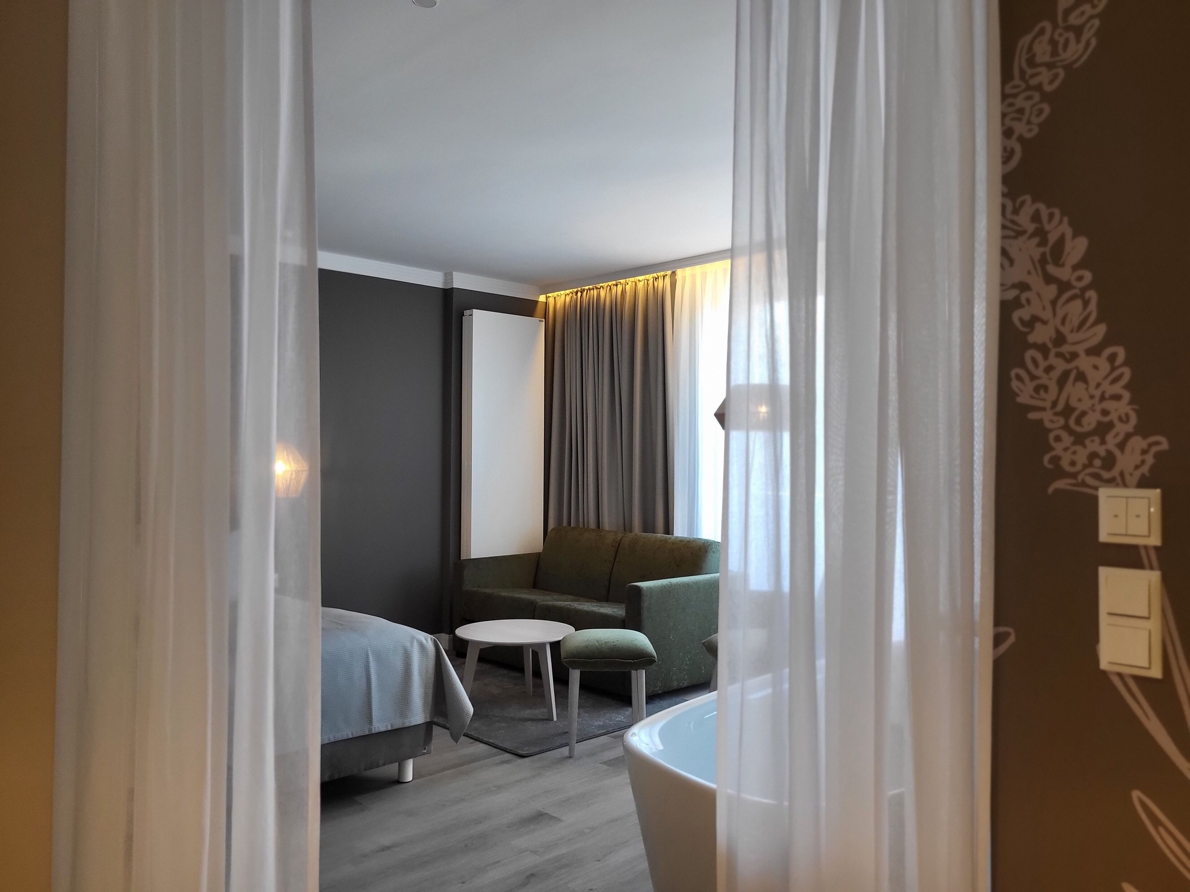 A modern hotel room with a bed, a sofa, a small round table, and a bathroom.