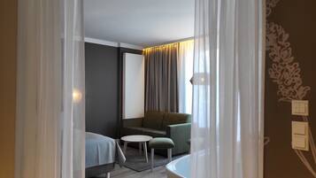 A modern hotel room with a bed, a sofa, a small round table, and a bathroom.